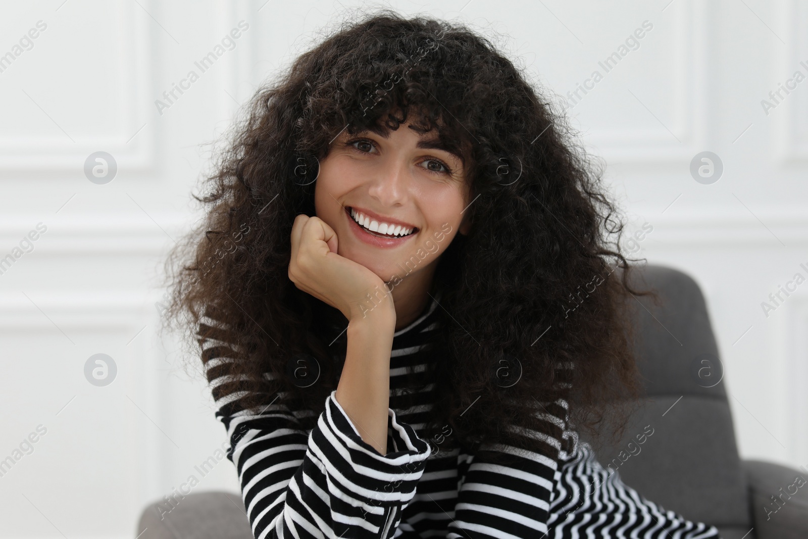 Photo of Portrait of beautiful woman with curly hair indoors. Attractive lady smiling and looking at camera