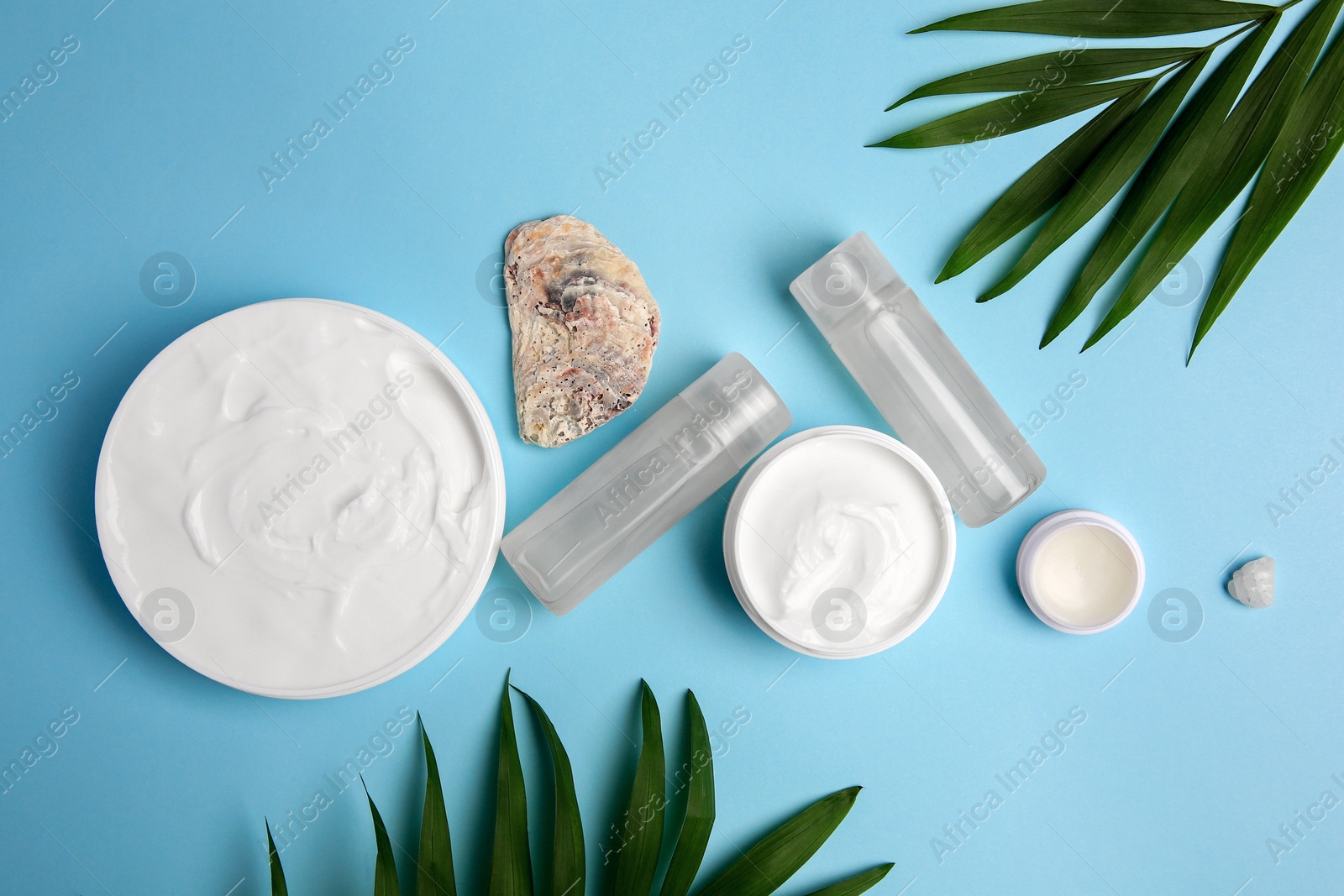 Photo of Flat lay composition with different cosmetic products and palm leaves on light blue background