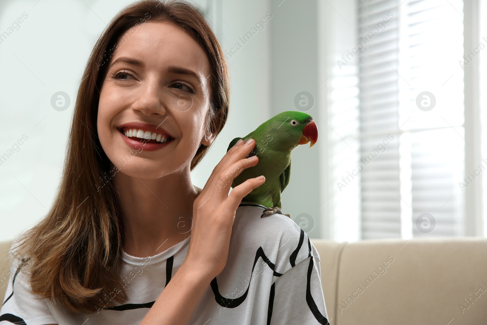 Photo of Young woman with cute Alexandrine parakeet indoors