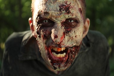 Scary zombie with bloody face outdoors, closeup. Halloween monster