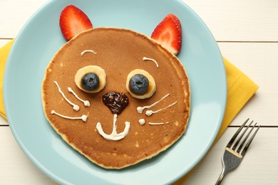 Photo of Creative serving for kids. Plate with cute cat made of pancakes, berries, cream, banana and chocolate paste on white wooden table, top view