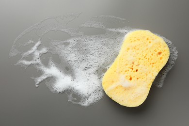 Yellow sponge with foam on grey background, top view