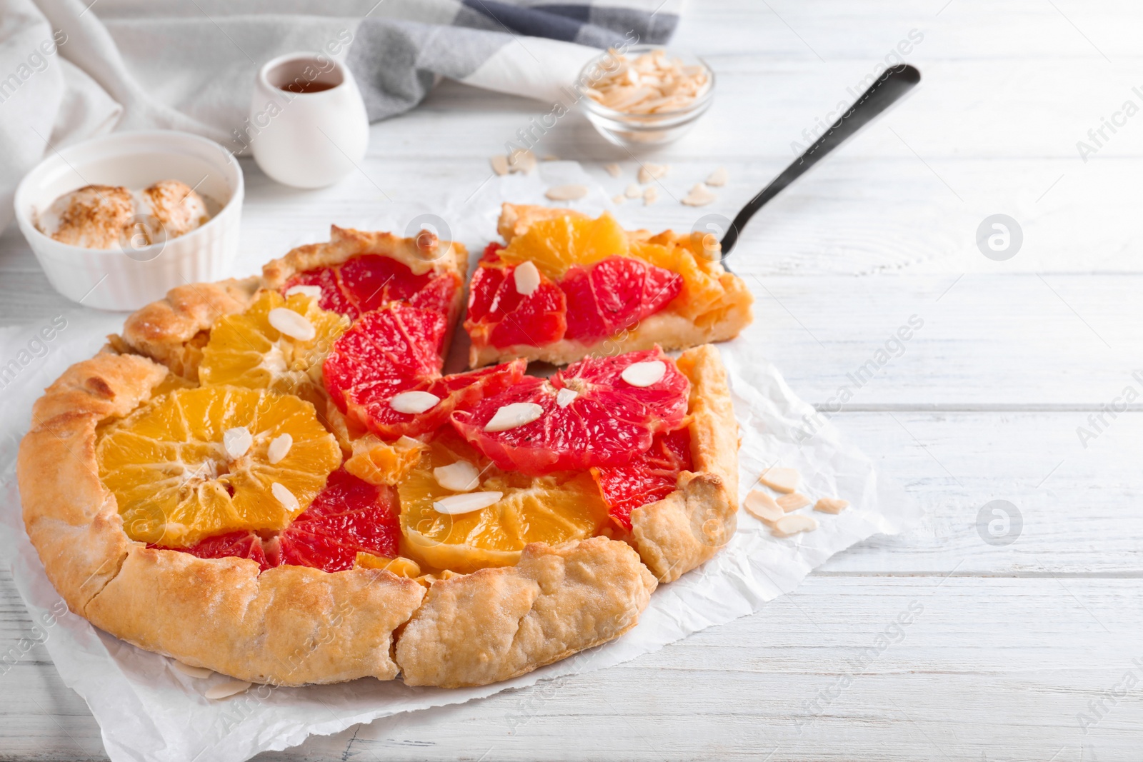 Photo of Tasty galette with citrus fruits and almond flakes on white table