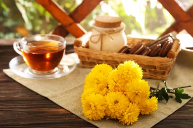 Photo of Beautiful yellow chrysanthemum flowers, cup of aromatic tea and sweet chocolate treats on wooden table. Space for text