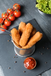Photo of Slate plate with basket of cheese sticks and sauce on table, closeup
