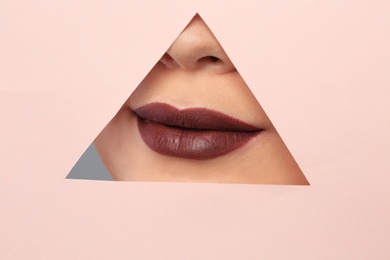 Lips of beautiful young woman with dark lipstick visible through hole in color paper