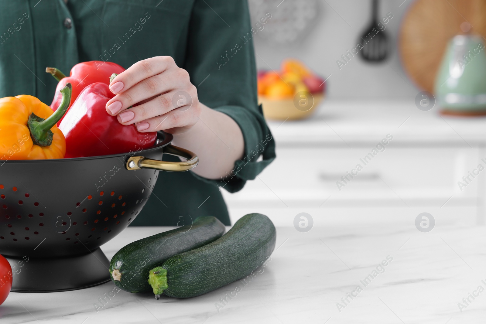 Photo of Woman taking bell pepper from black colander at white marble table in kitchen, closeup. Space for text