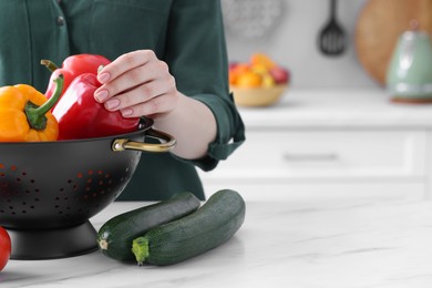 Photo of Woman taking bell pepper from black colander at white marble table in kitchen, closeup. Space for text