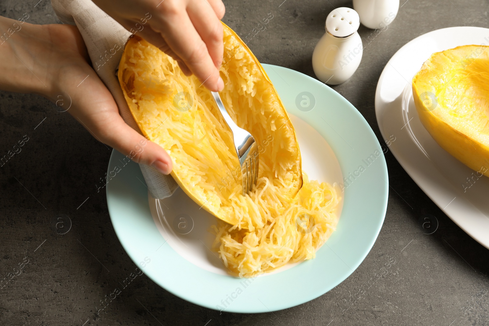 Photo of Woman scraping flesh of cooked spaghetti squash with fork on table, closeup