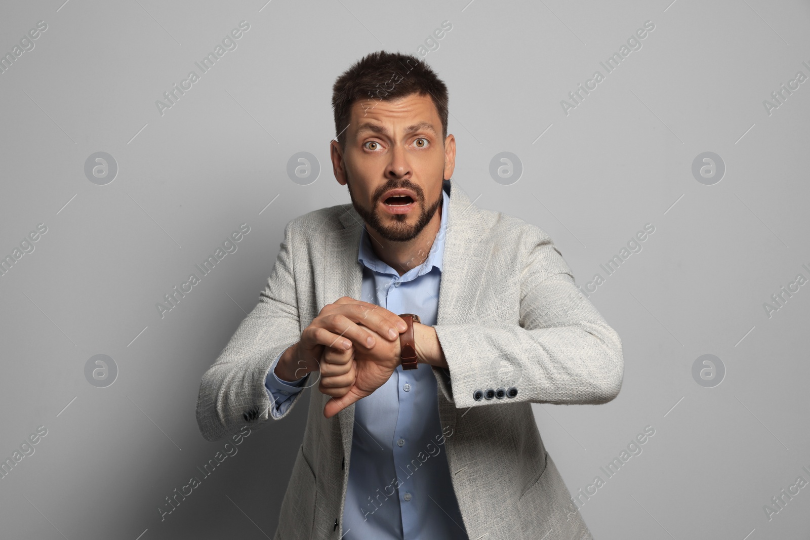 Photo of Emotional man checking time on grey background. Being late concept