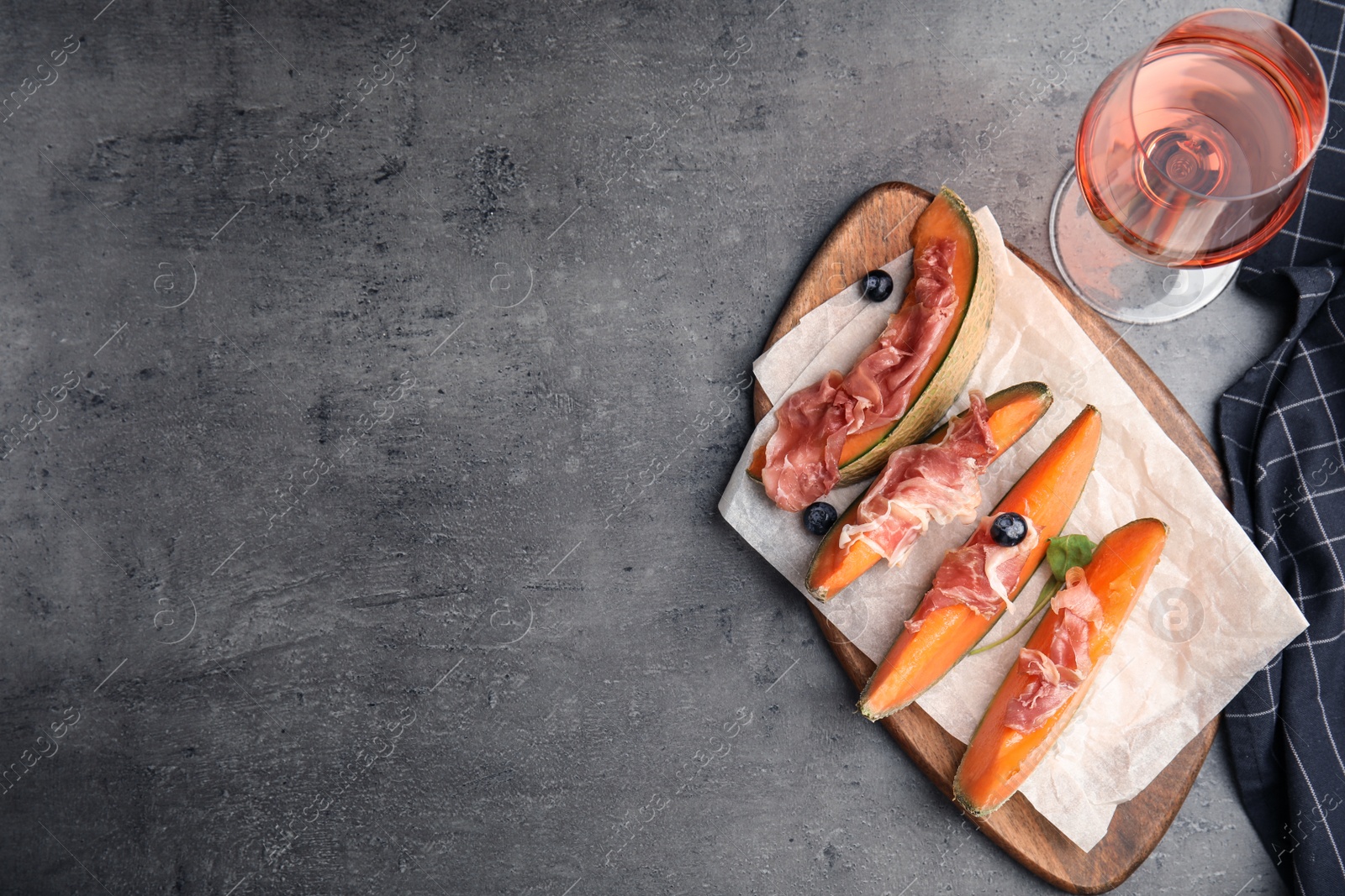 Photo of Flat lay composition of fresh melon with prosciutto on grey table. Space for text