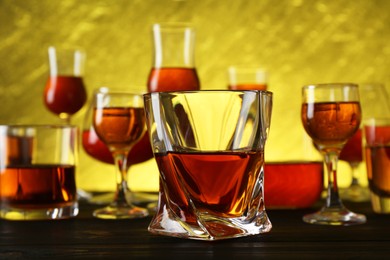 Photo of Different delicious liqueurs in glasses on dark wooden table