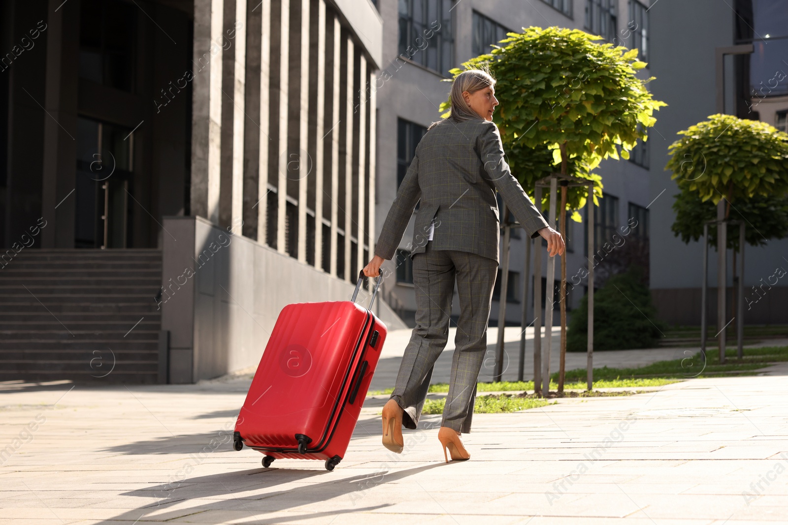 Photo of Being late. Senior businesswoman with red suitcase running outdoors, low angle view