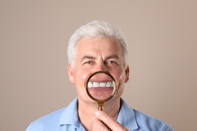 Photo of Mature man with healthy teeth and magnifier on color background