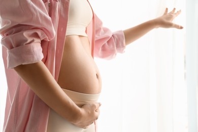 Photo of Pregnant young woman touching belly on light background, closeup. Space for text