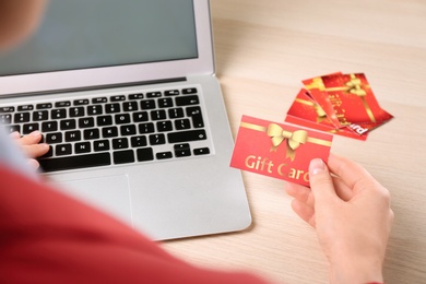 Photo of Woman with gift card and laptop at wooden table, closeup