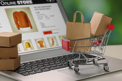 Photo of Mini shopping bag, boxes and cart on laptop, closeup. Online store