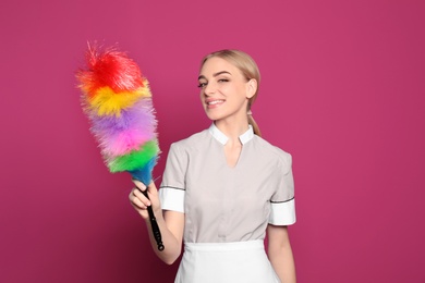 Photo of Young chambermaid with dusting brush on color background