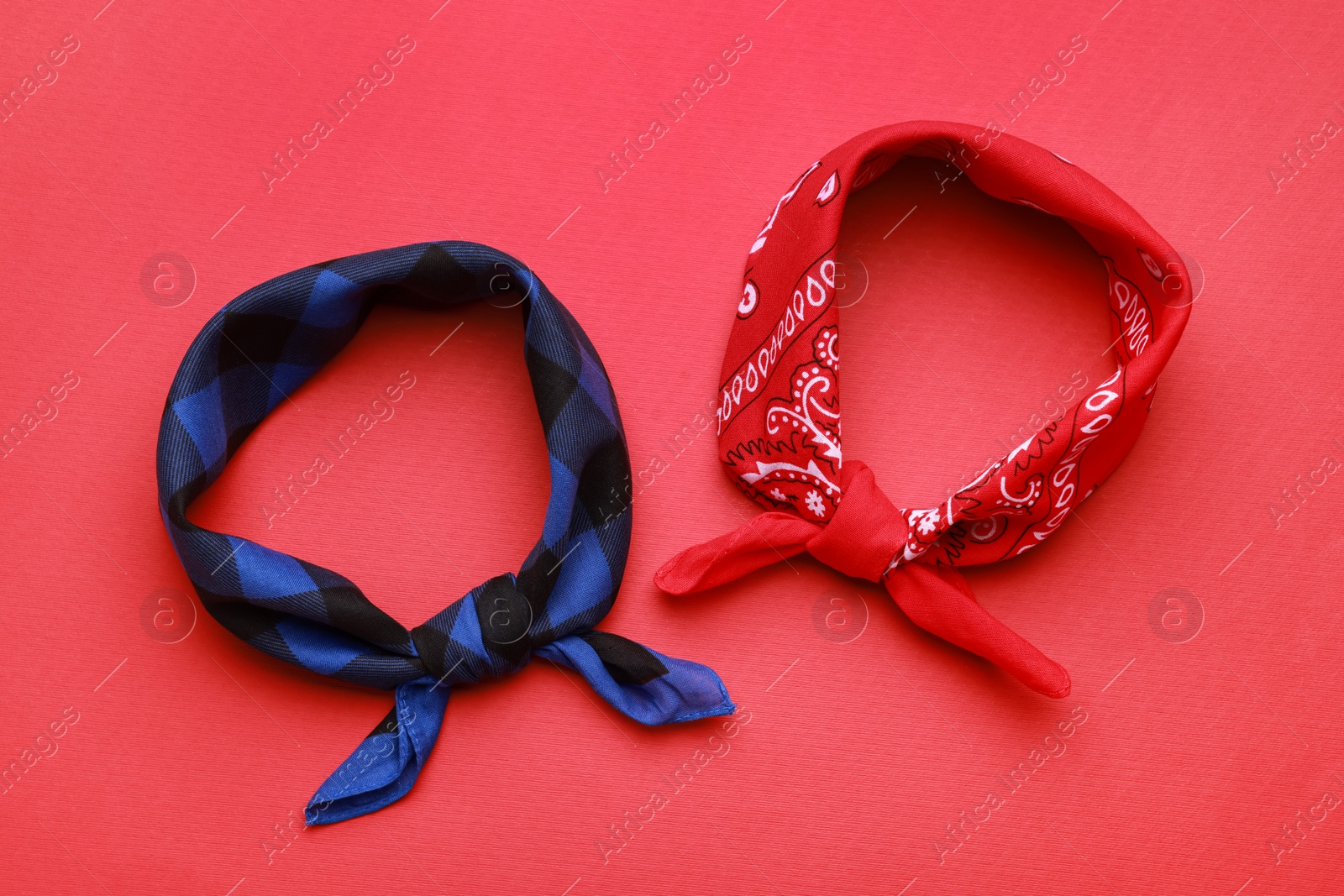 Photo of Tied bandanas with different patterns on red background, flat lay