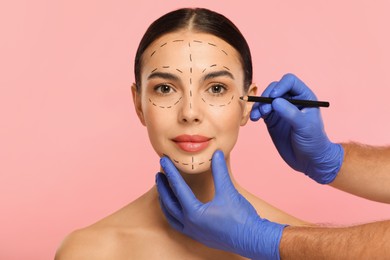 Photo of Doctor with pencil preparing patient for cosmetic surgery operation on pink background