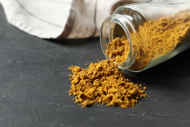 Photo of Jar with dry curry powder on dark textured table, closeup. Space for text