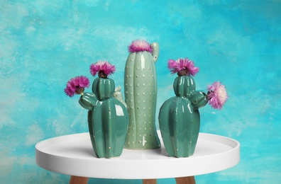 Photo of Trendy cactus shaped ceramic vases with flowers on table