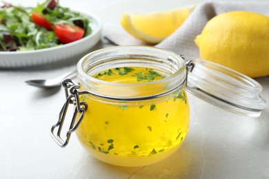 Photo of Jar with lemon sauce on light table, closeup. Delicious salad dressing