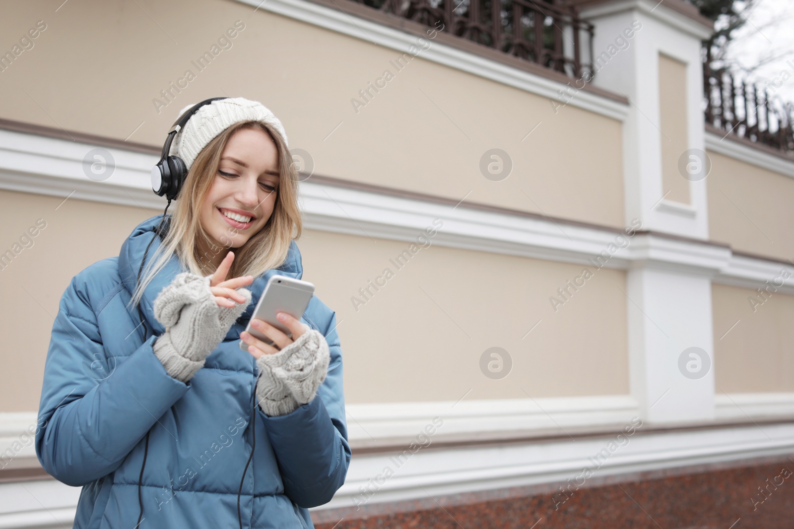 Photo of Young woman with headphones listening to music near light wall. Space for text