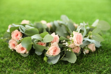 Wreath made of beautiful flowers on green grass outdoors, closeup