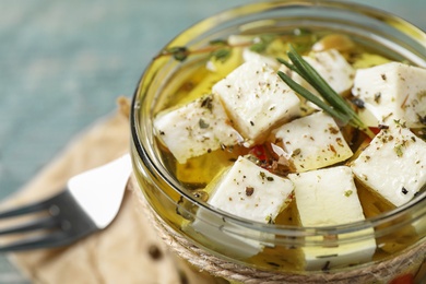 Photo of Pickled feta cheese in jar on blue table, closeup