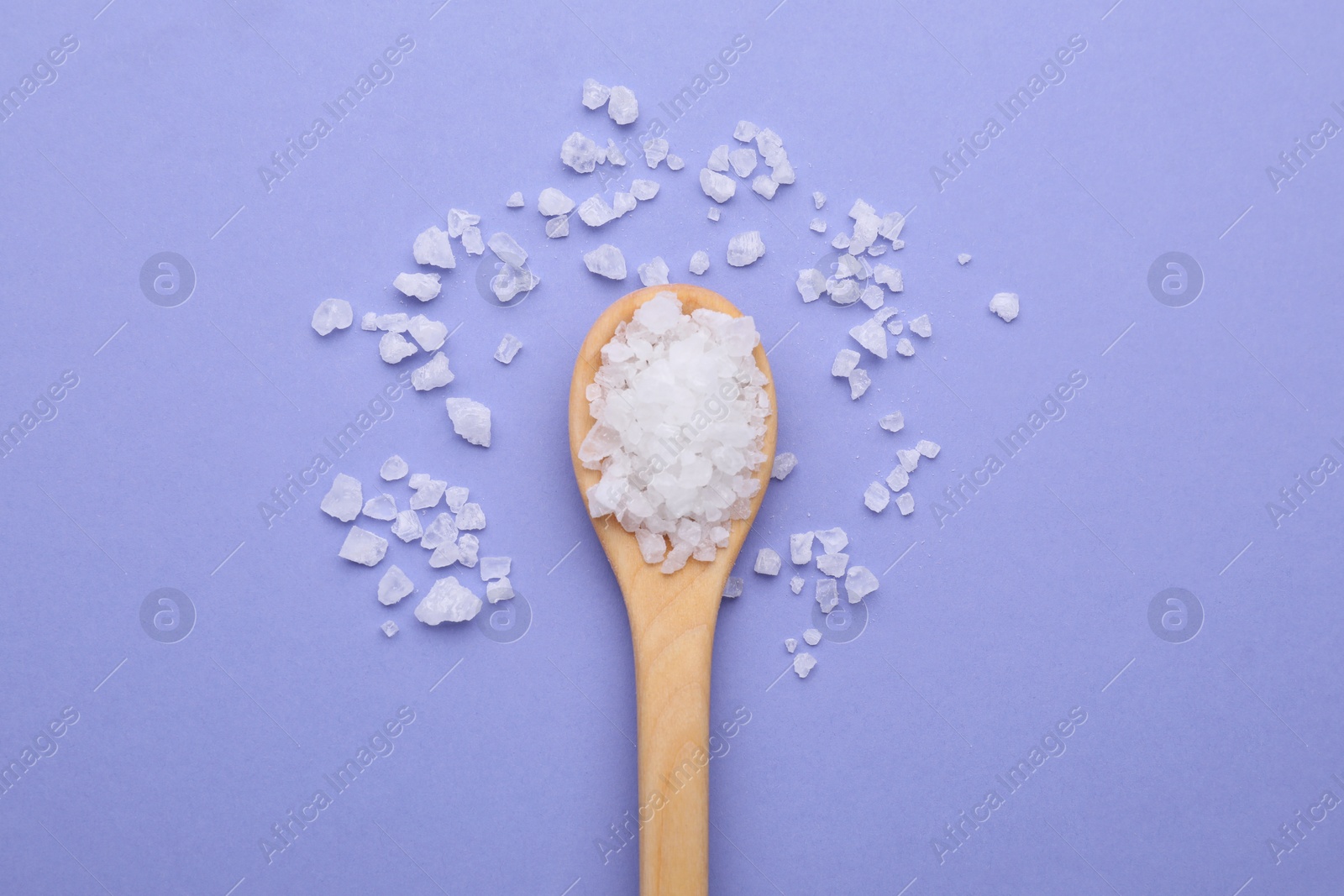 Photo of Spoon with sea salt on violet background, top view