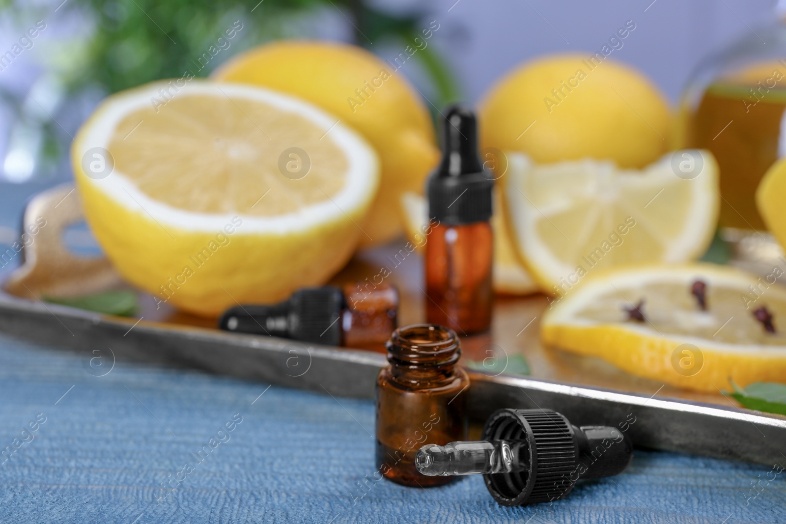 Photo of Bottle with essential oil and blurred lemons on background, closeup