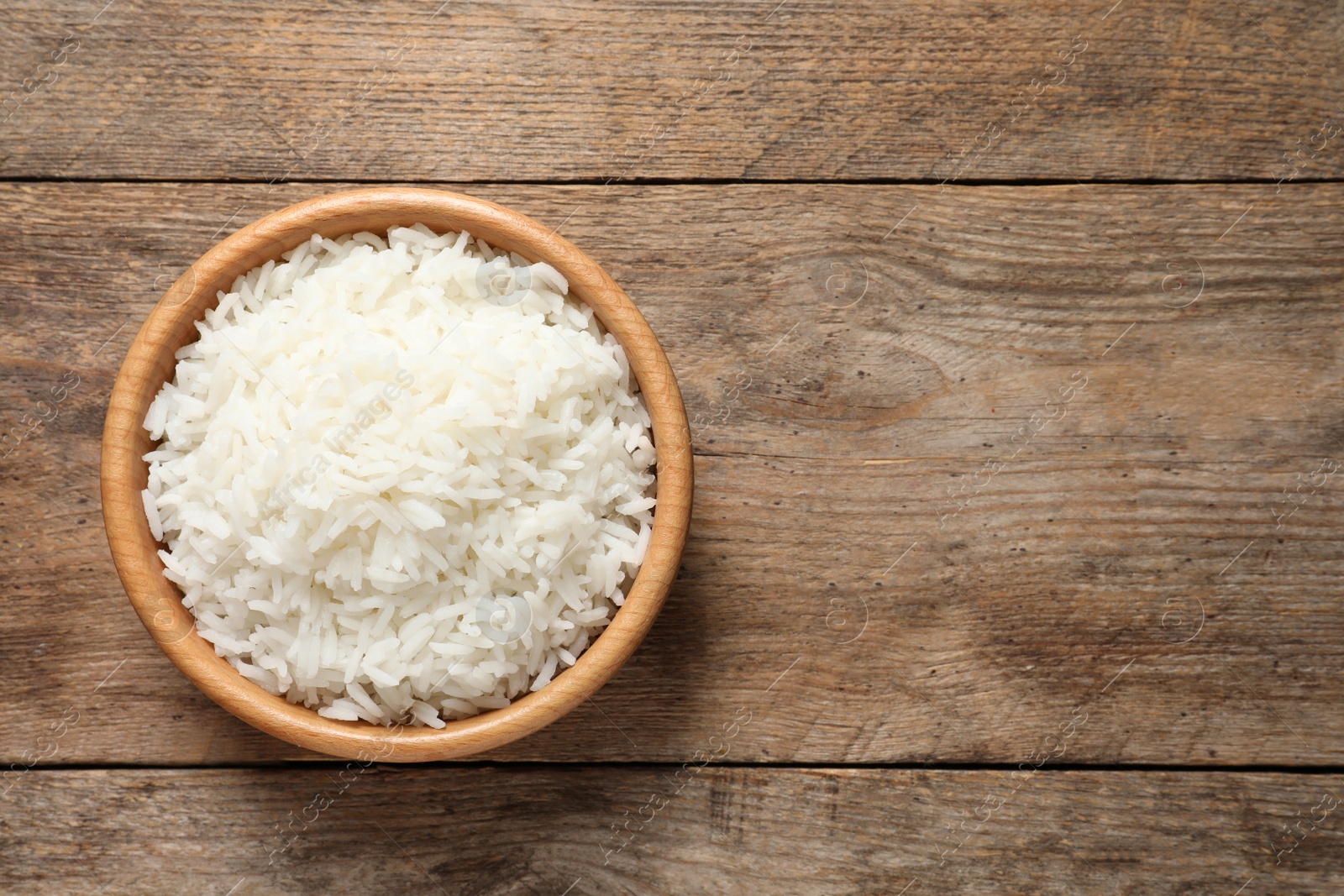 Photo of Bowl of delicious rice on wooden table, top view with space for text