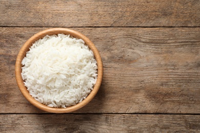 Bowl of delicious rice on wooden table, top view with space for text