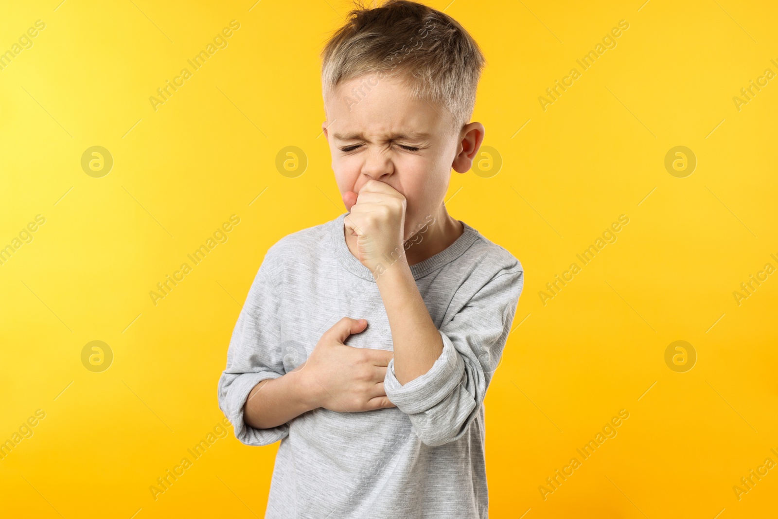 Photo of Sick boy coughing on yellow background. Cold symptoms