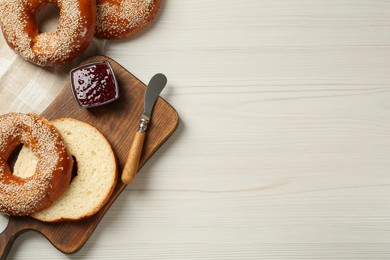 Photo of Delicious fresh bagels with sesame seeds and jam on white wooden table, flat lay. Space for text