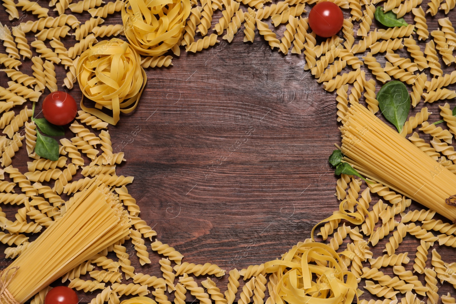 Photo of Frame of pasta, basil and tomatoes on wooden table, space or text
