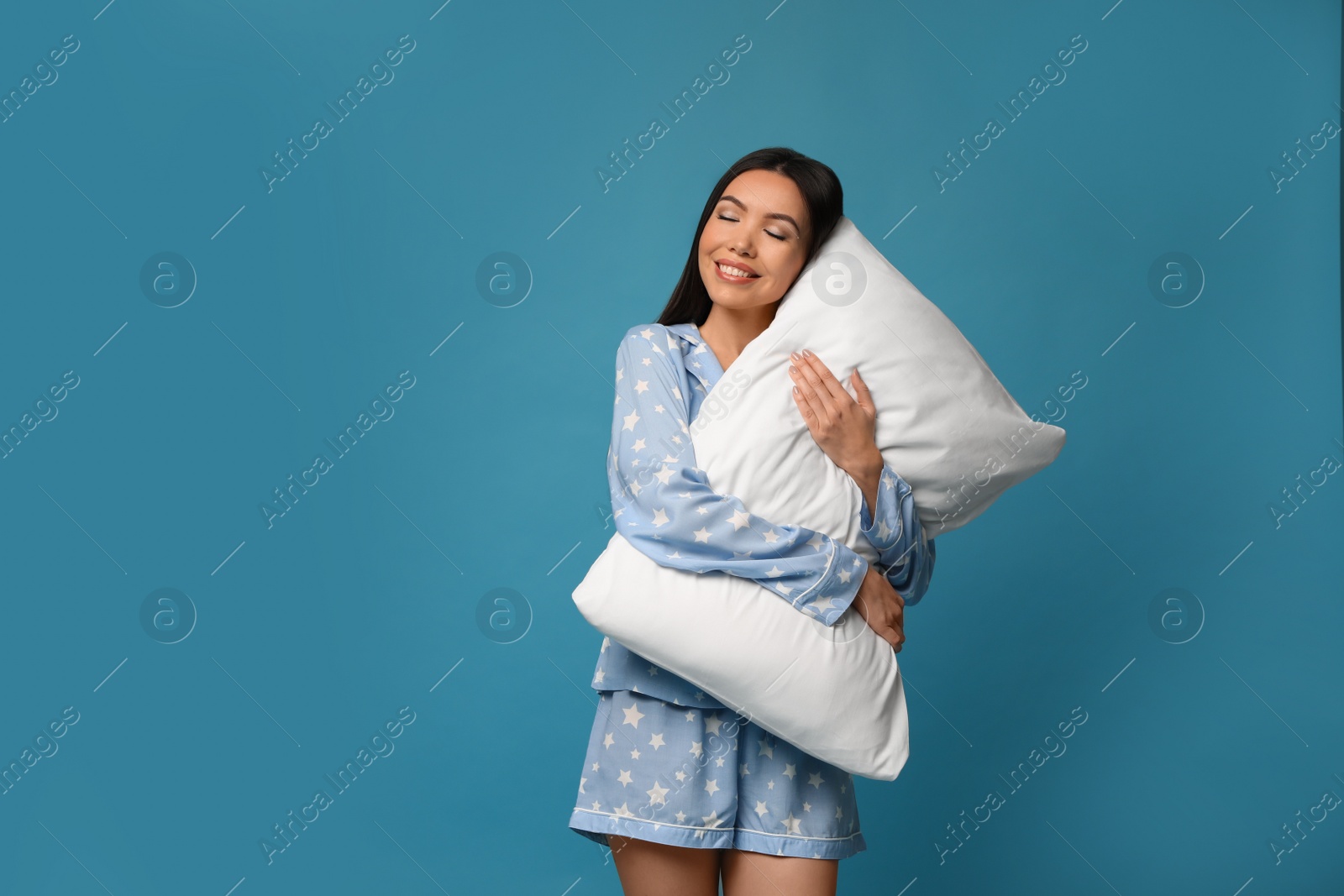 Photo of Beautiful Asian woman with pillow on blue background. Bedtime