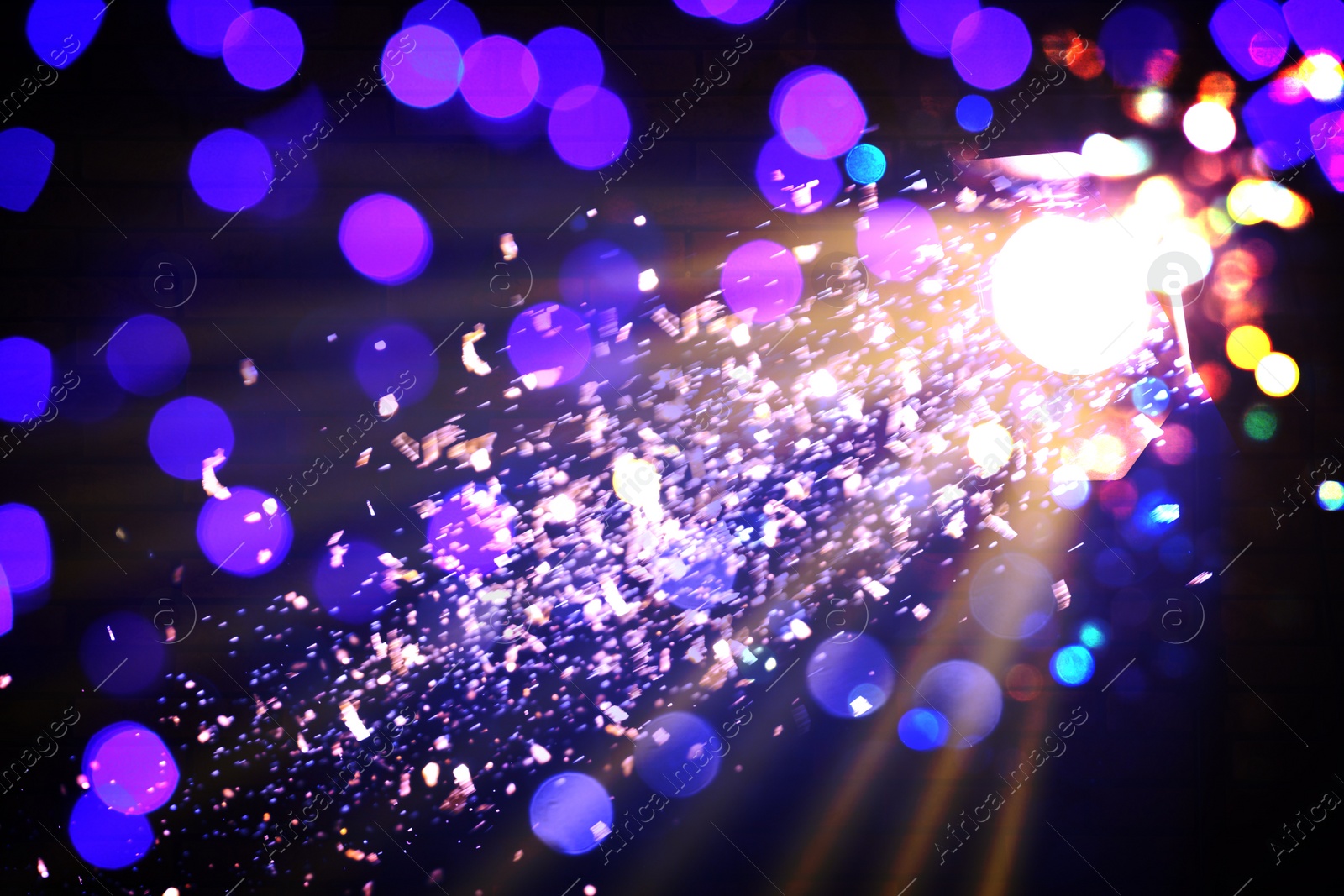 Image of Bright spotlight, beams of light and falling shiny confetti in darkness of night club, bokeh effect