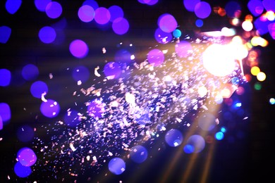 Image of Bright spotlight, beams of light and falling shiny confetti in darkness of night club, bokeh effect