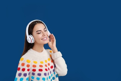 Young woman listening to music with headphones on dark blue background, space for text