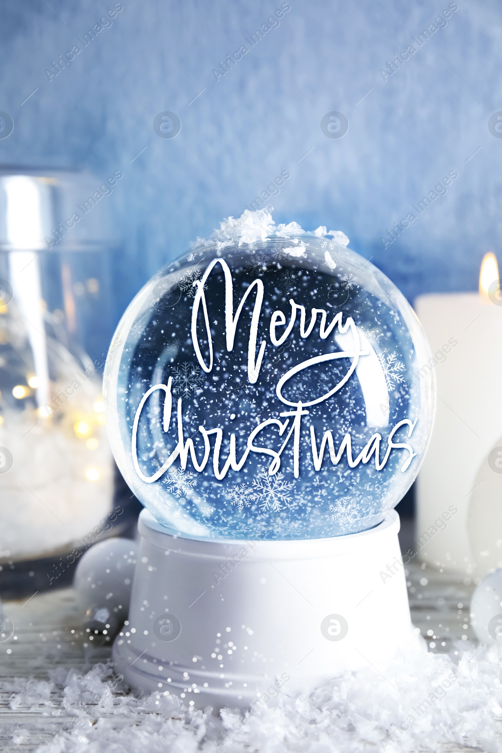 Beautiful snow globe with phrase Merry Christmas and decorations and candles on table Image of Beautiful snow globe with phrase Merry Christmas and decorations and candles on table