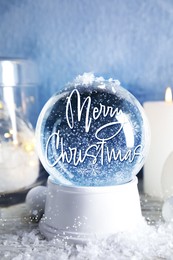 Image of Beautiful snow globe with phrase Merry Christmas and decorations and candles on table