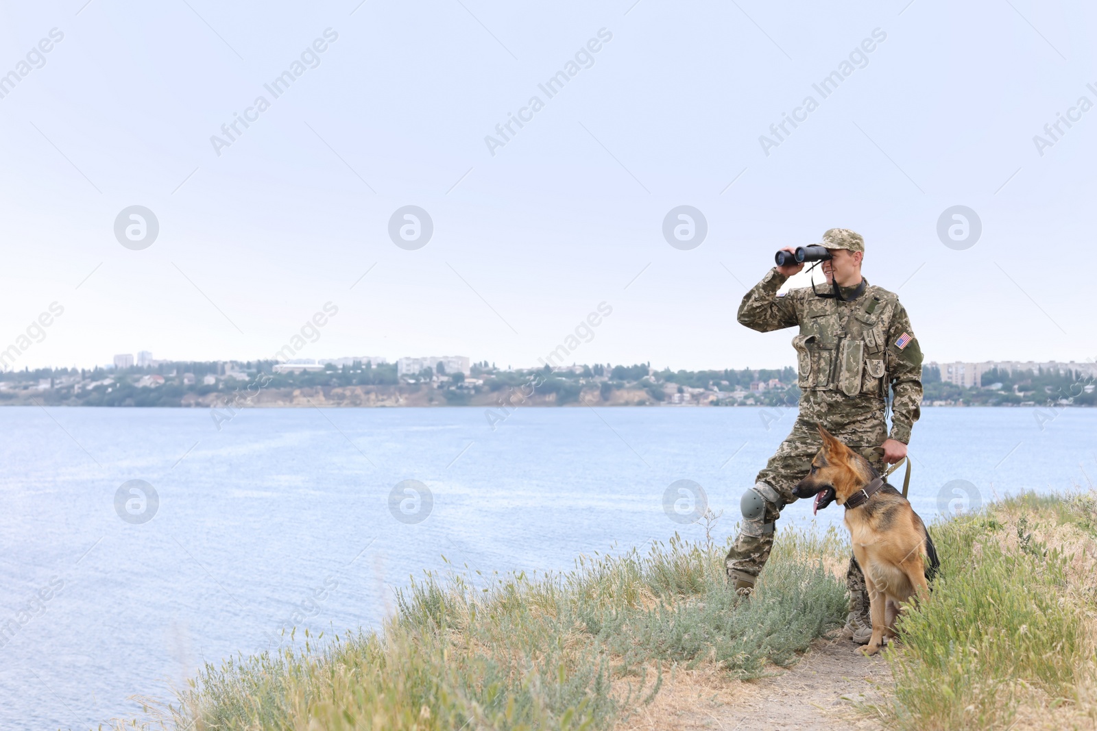 Photo of Man in military uniform with German shepherd dog near river