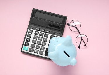 Calculator, glasses and piggy bank on pink background, flat lay