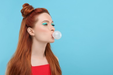 Beautiful woman with bright makeup blowing bubble gum on light blue background. Space for text