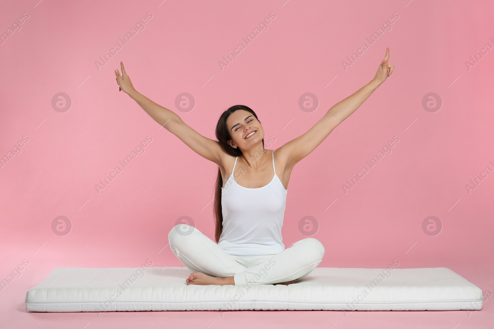 Photo of Young woman stretching on soft mattress against pink background