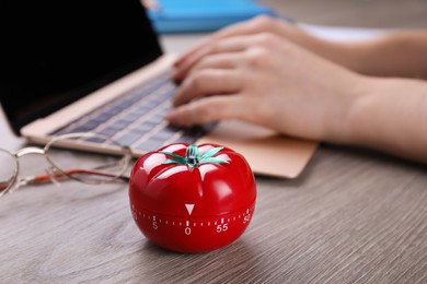 Woman working on laptop at wooden table, focus on kitchen timer in shape of tomato. Space for text