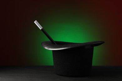 Photo of Magician's hat and wand on black wooden table against dark background