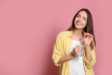 Photo of Young woman with glass of lemon water on pink background. Space for text